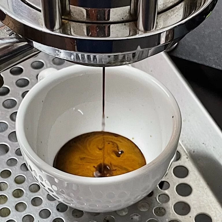 Espresso extracting from a bottomless portafilter into a white dimpled cup